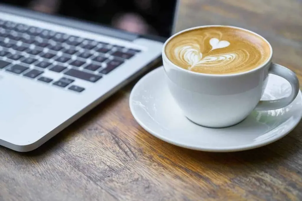 A laptop and a flat white on a wooden desk