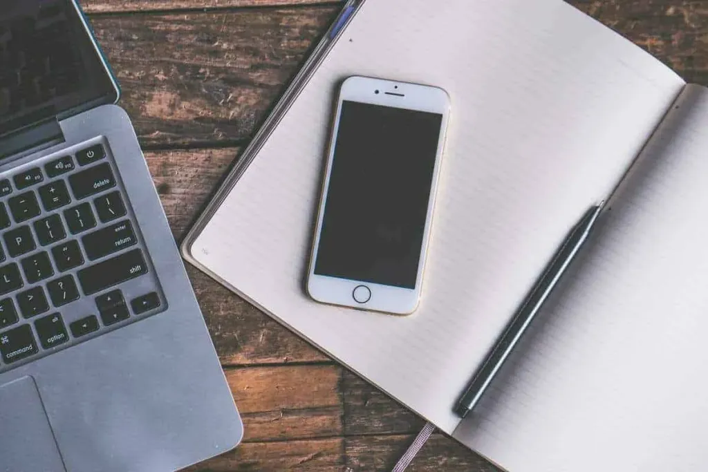 A laptop, phone and notebook on a desk